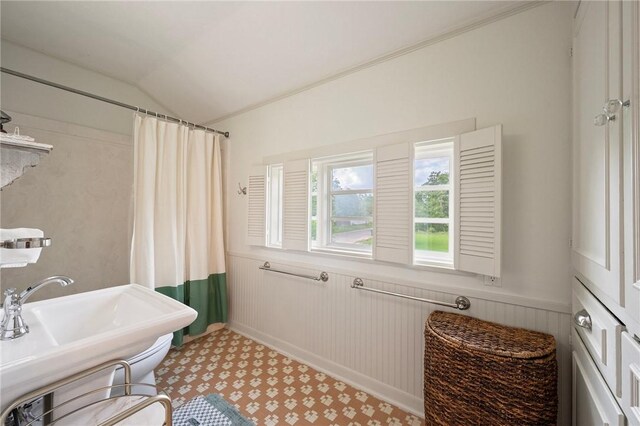 full bath featuring curtained shower, a wainscoted wall, and vaulted ceiling