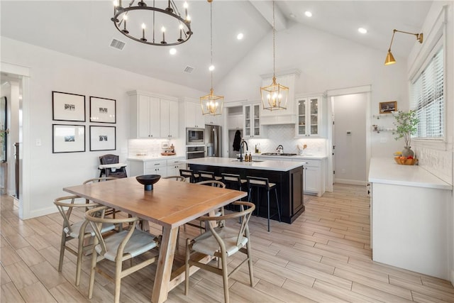 kitchen featuring tasteful backsplash, stainless steel appliances, white cabinets, decorative light fixtures, and a kitchen island with sink