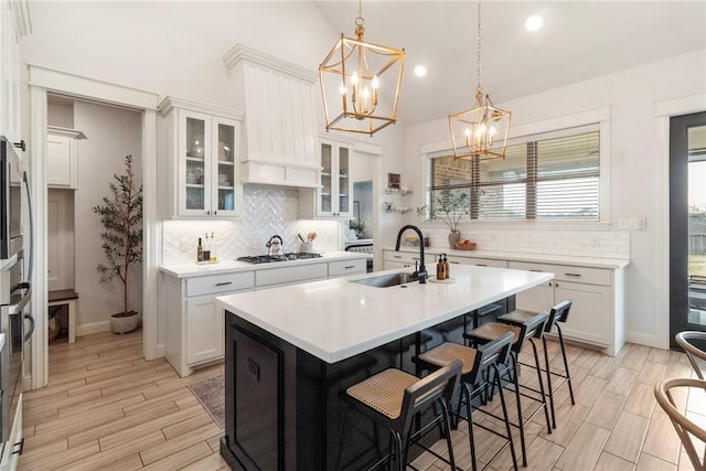 kitchen featuring a kitchen island with sink, hanging light fixtures, sink, white cabinets, and a kitchen breakfast bar