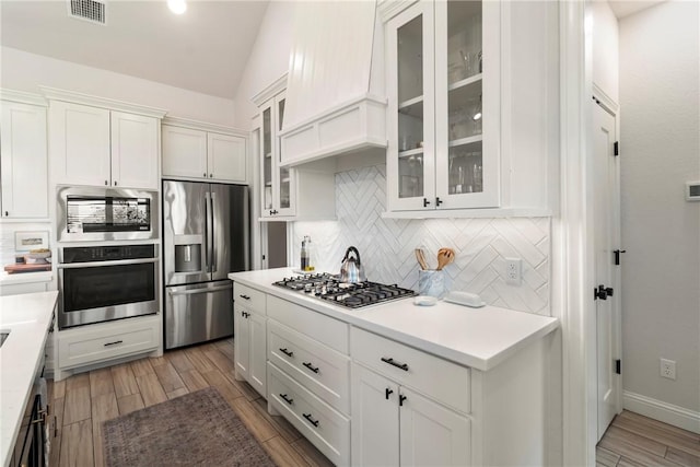 kitchen featuring appliances with stainless steel finishes, decorative backsplash, white cabinetry, and premium range hood