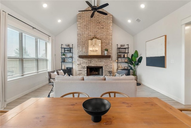 dining area with vaulted ceiling, a brick fireplace, ceiling fan, and light hardwood / wood-style flooring