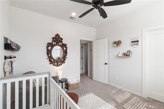 carpeted bedroom featuring a nursery area and ceiling fan