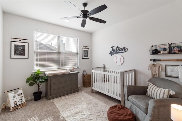 bedroom featuring ceiling fan, a nursery area, and light colored carpet