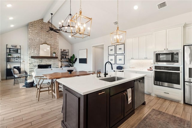 kitchen with sink, decorative light fixtures, stainless steel appliances, a fireplace, and white cabinets