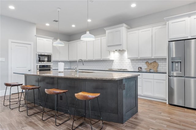 kitchen featuring dark stone countertops, white cabinetry, stainless steel appliances, and an island with sink