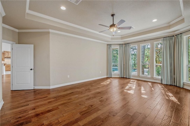 empty room with hardwood / wood-style floors, ceiling fan, a raised ceiling, and ornamental molding