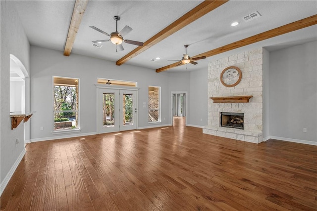 unfurnished living room featuring hardwood / wood-style floors, a stone fireplace, ceiling fan, a textured ceiling, and beamed ceiling