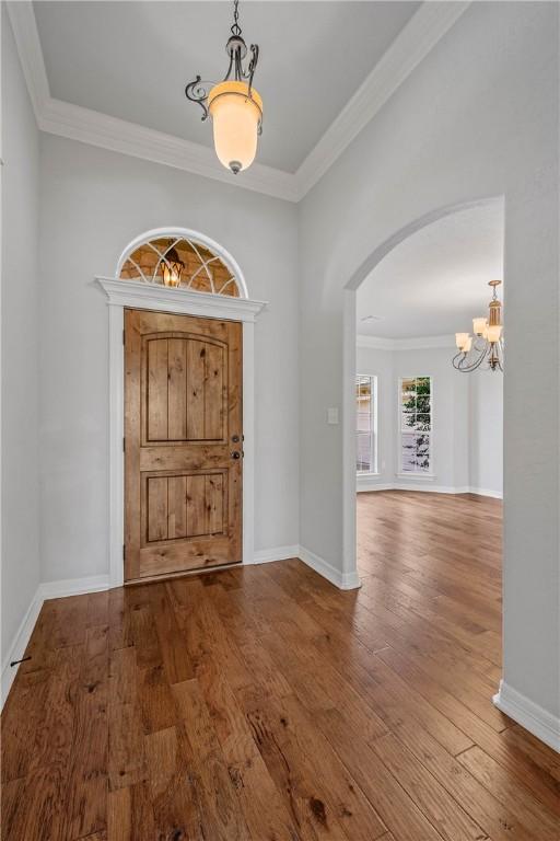 foyer featuring wood-type flooring, crown molding, and a chandelier