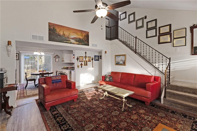 living room with wood-type flooring, ceiling fan with notable chandelier, and high vaulted ceiling