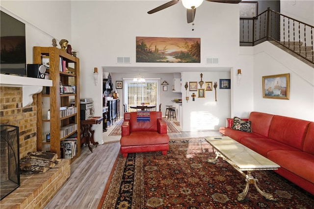 living room featuring a fireplace, a towering ceiling, hardwood / wood-style flooring, and ceiling fan with notable chandelier