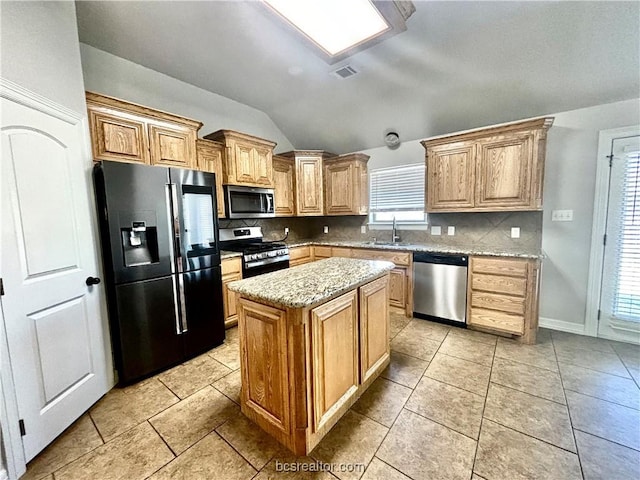 kitchen featuring vaulted ceiling, tasteful backsplash, a kitchen island, light stone counters, and stainless steel appliances