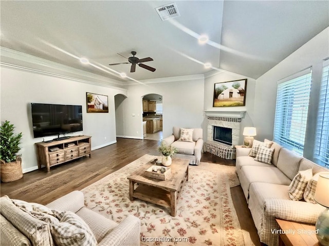 living room featuring a brick fireplace, vaulted ceiling, ceiling fan, crown molding, and dark wood-type flooring