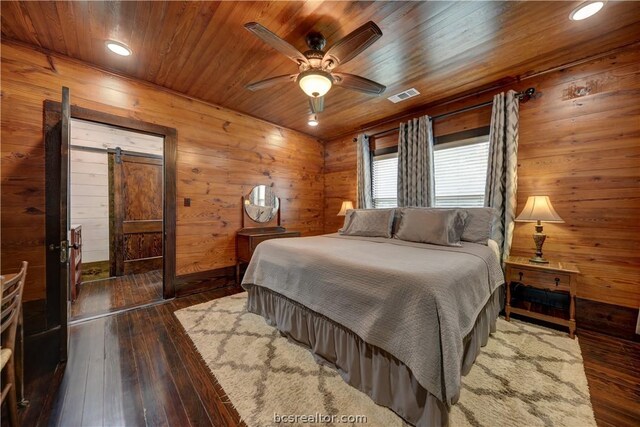 bedroom with wooden ceiling, dark wood-type flooring, wooden walls, ceiling fan, and a barn door