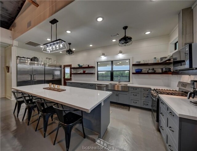 kitchen with a kitchen breakfast bar, stainless steel appliances, sink, decorative light fixtures, and a kitchen island