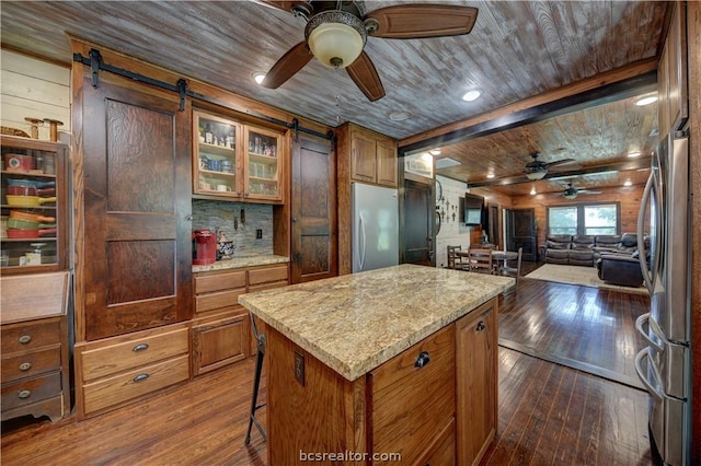 kitchen featuring dark wood-type flooring, a barn door, a kitchen island, light stone counters, and stainless steel refrigerator