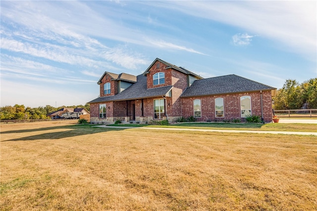 view of front of house with brick siding, roof with shingles, a front lawn, and fence