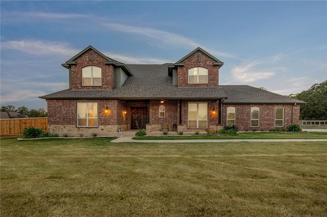 traditional home featuring brick siding, a shingled roof, a front lawn, and fence