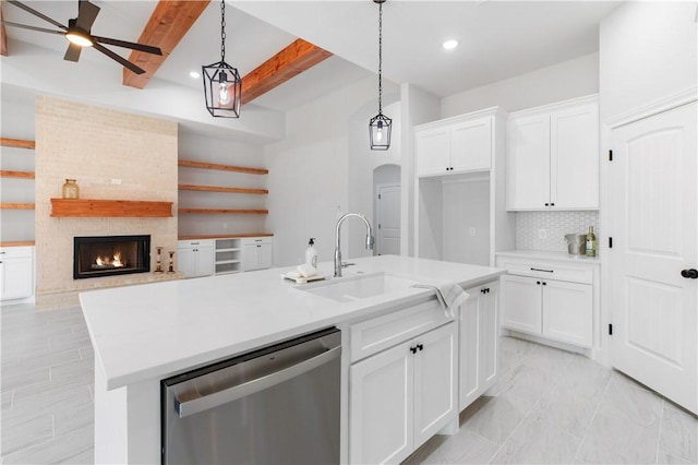 kitchen featuring arched walkways, stainless steel dishwasher, a fireplace, white cabinetry, and backsplash