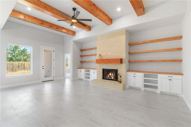 unfurnished living room featuring a large fireplace, baseboards, beam ceiling, and recessed lighting