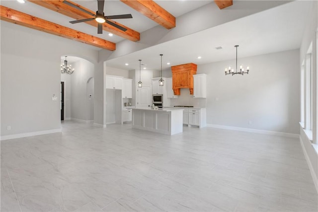 unfurnished living room with arched walkways, recessed lighting, ceiling fan with notable chandelier, baseboards, and beamed ceiling
