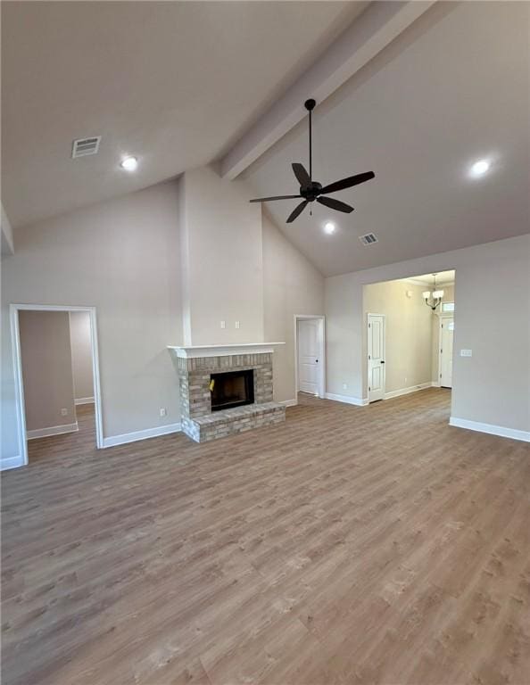 unfurnished living room featuring high vaulted ceiling, a brick fireplace, light wood-type flooring, beamed ceiling, and ceiling fan with notable chandelier