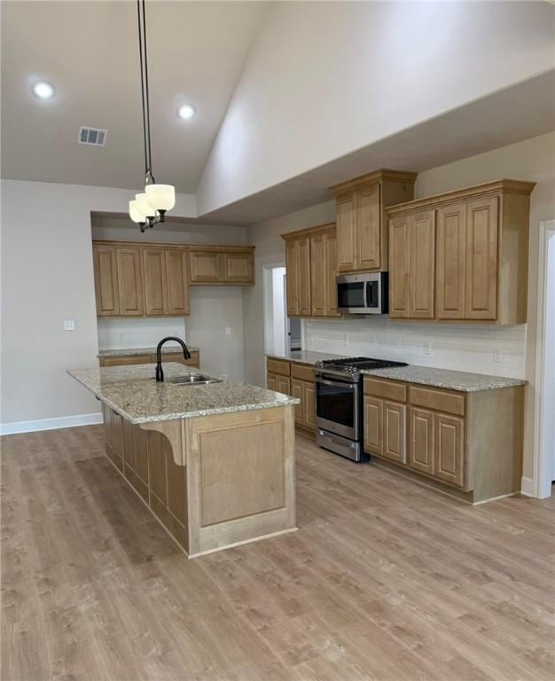 kitchen featuring sink, appliances with stainless steel finishes, hanging light fixtures, light stone counters, and an island with sink