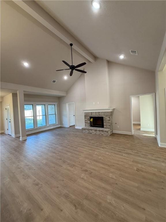 unfurnished living room with vaulted ceiling with beams, ceiling fan, a brick fireplace, and light wood-type flooring