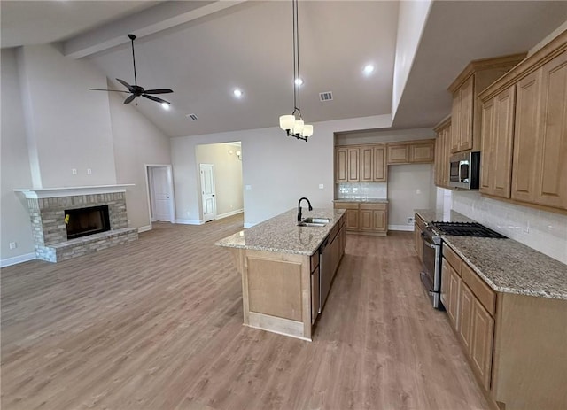 kitchen with a center island with sink, pendant lighting, stainless steel appliances, light stone countertops, and backsplash