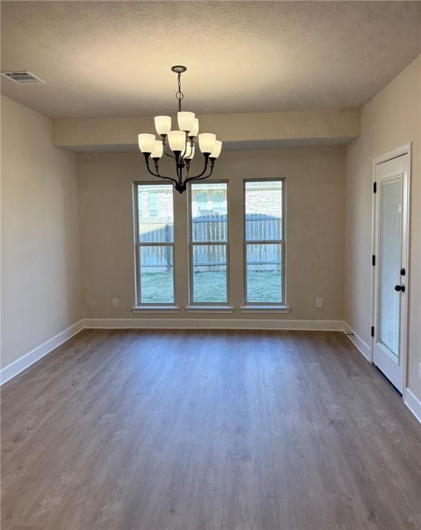 unfurnished room with an inviting chandelier, dark hardwood / wood-style floors, and a healthy amount of sunlight