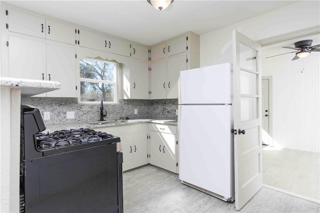 kitchen featuring sink, white cabinets, black gas range oven, and white refrigerator