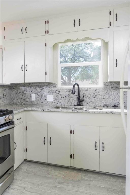 kitchen with white cabinets, decorative backsplash, stainless steel range with gas cooktop, and sink