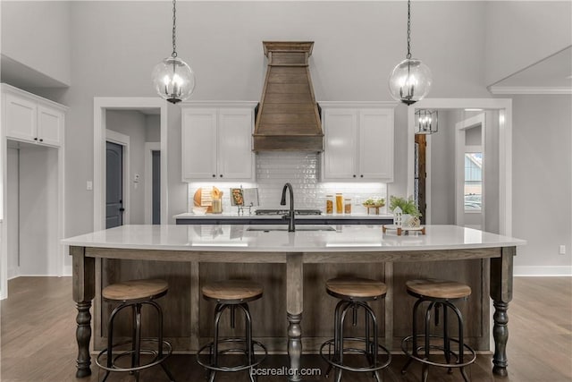 kitchen with a kitchen island with sink, white cabinets, and custom exhaust hood