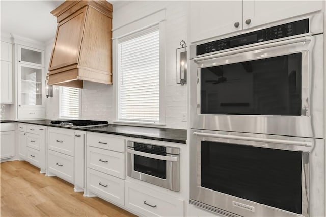 1701 Kerr Valley Ln, College Station, TX 77845 - kitchen with stainless steel appliances, custom range hood, light wood-type flooring, dark countertops, and white cabinets