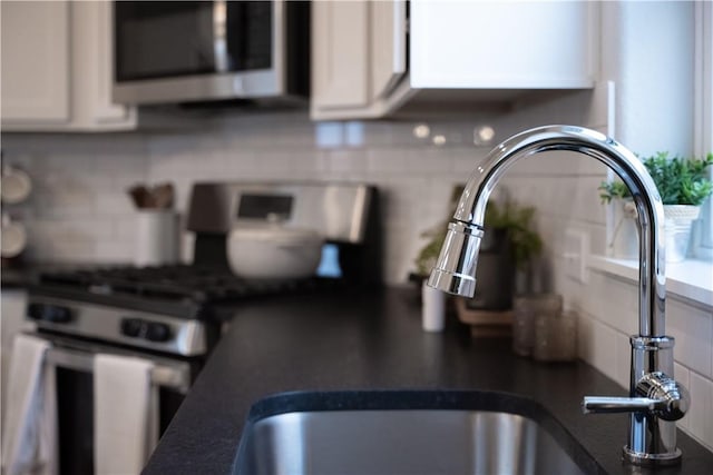 room details with dark countertops, a sink, decorative backsplash, appliances with stainless steel finishes, and white cabinetry