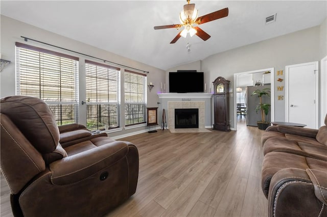 living room featuring visible vents, light wood-style flooring, a ceiling fan, a fireplace, and lofted ceiling