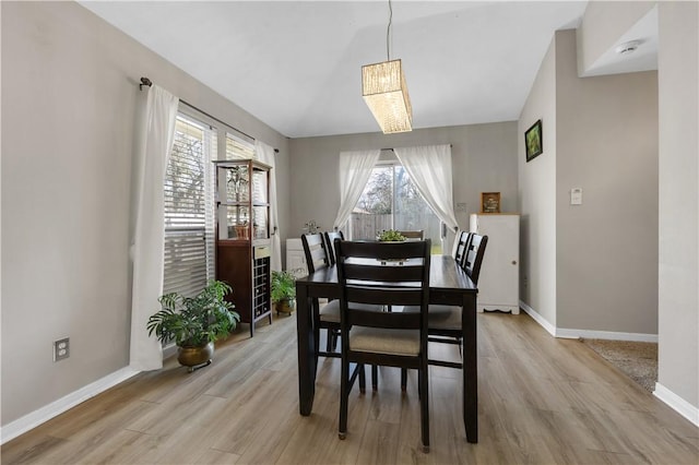 dining area featuring vaulted ceiling, light wood-style floors, and baseboards