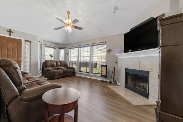 living room with baseboards, ceiling fan, vaulted ceiling, light wood-style flooring, and a tile fireplace