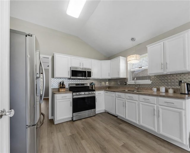 kitchen with lofted ceiling, decorative backsplash, white cabinets, stainless steel appliances, and a sink