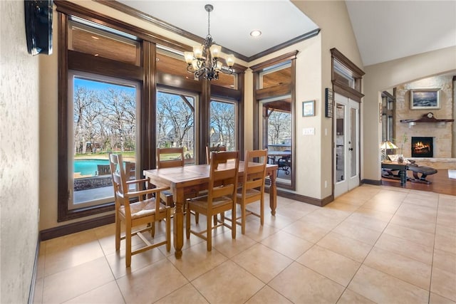 dining area featuring lofted ceiling, light tile patterned flooring, a stone fireplace, a chandelier, and baseboards