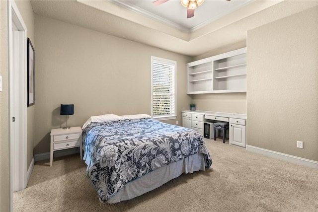 bedroom featuring light carpet, baseboards, built in study area, a tray ceiling, and crown molding