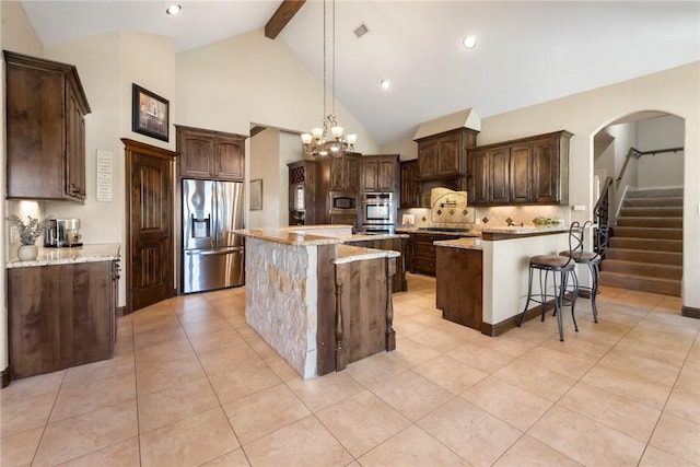 kitchen featuring a center island, stainless steel appliances, visible vents, dark brown cabinets, and light stone countertops