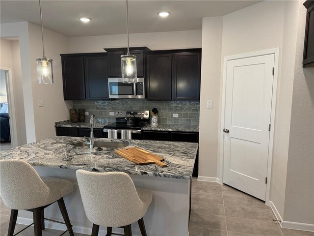 kitchen featuring sink, a kitchen island with sink, stainless steel appliances, pendant lighting, and decorative backsplash