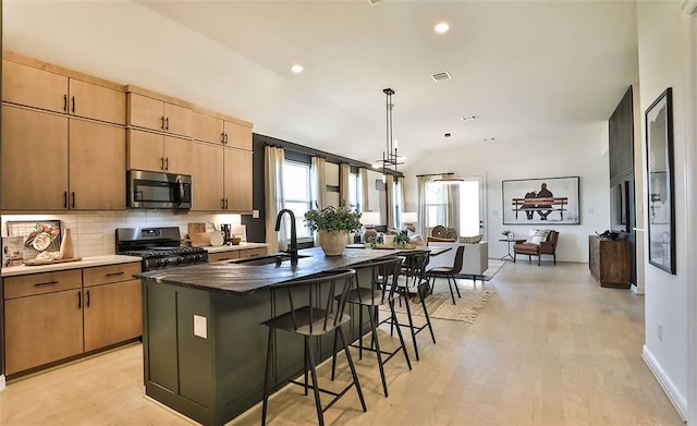 kitchen featuring stainless steel microwave, stove, a kitchen island with sink, a kitchen bar, and a sink