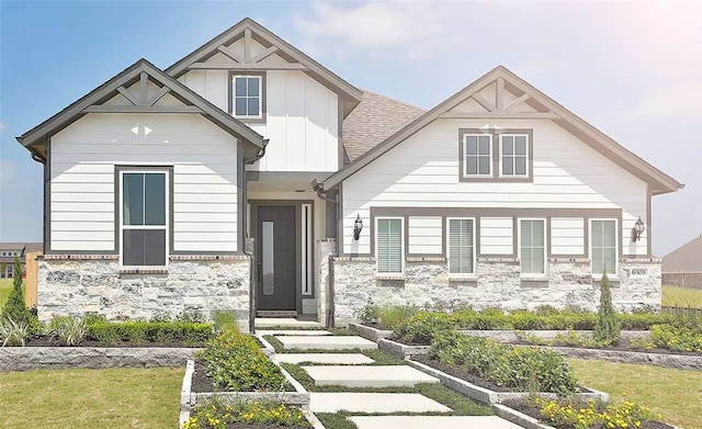 view of front of house featuring a shingled roof, stone siding, a vegetable garden, board and batten siding, and a front yard