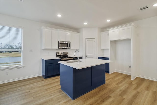 kitchen featuring appliances with stainless steel finishes, sink, white cabinets, a kitchen island with sink, and light hardwood / wood-style flooring