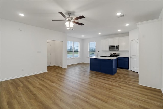 kitchen featuring blue cabinetry, appliances with stainless steel finishes, white cabinetry, light hardwood / wood-style floors, and a center island with sink