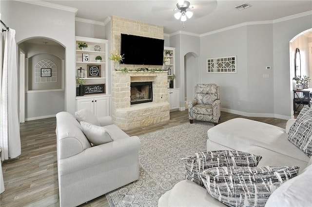 living room with arched walkways, crown molding, visible vents, a stone fireplace, and wood finished floors