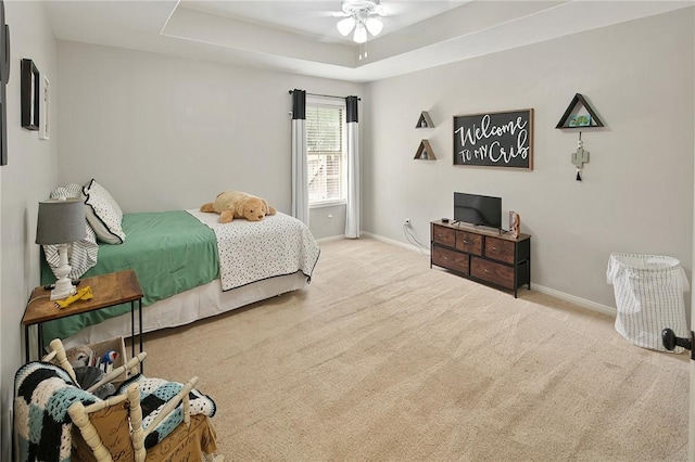 carpeted bedroom featuring baseboards, a tray ceiling, and a ceiling fan