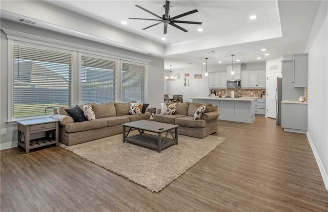 living room with a tray ceiling, ceiling fan with notable chandelier, and light wood-type flooring