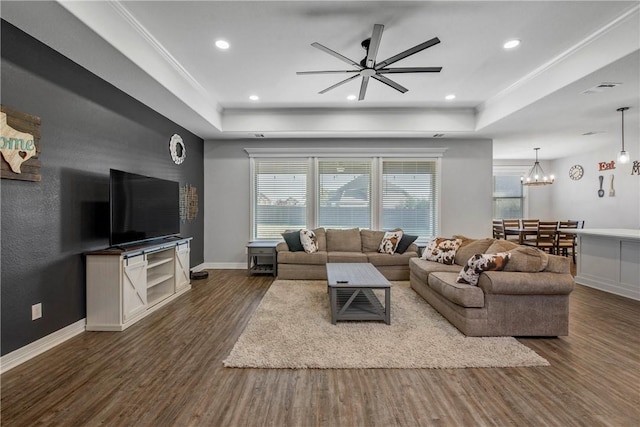 living room with a raised ceiling, ceiling fan with notable chandelier, dark hardwood / wood-style flooring, and ornamental molding